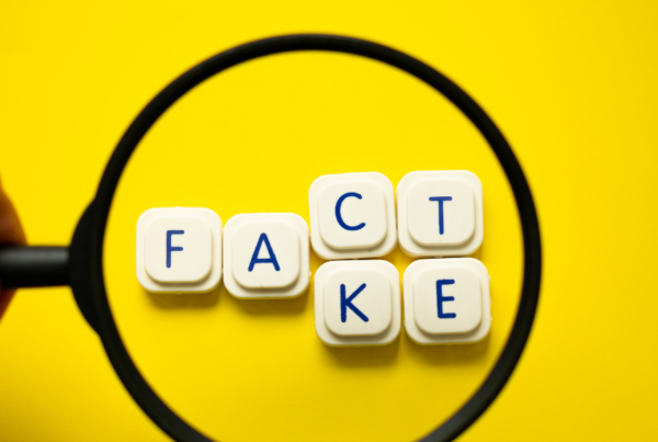 Person's Hand with Magnifying Glass with Fact and Fake Text